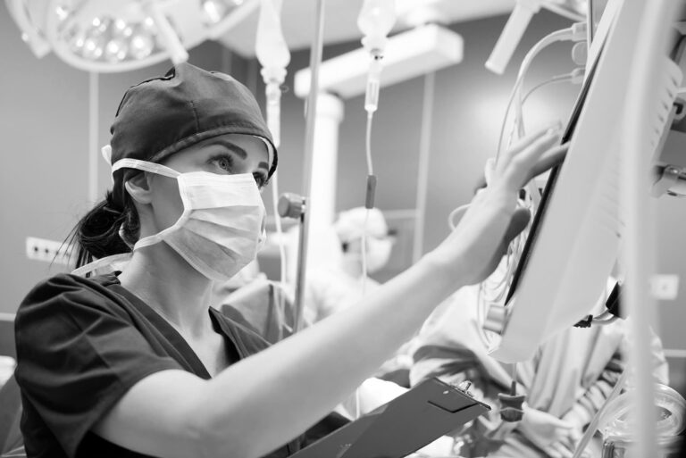 A nurse wearing a mask reviewing the notes on a monitor during surgery